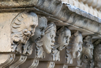 Closeup view of mascarons with funny faces under the balcony of a baroque palace in the province of Syracuse, Sicily