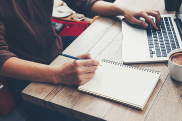 Young business man hand writing notebook and using laptop on wood table.