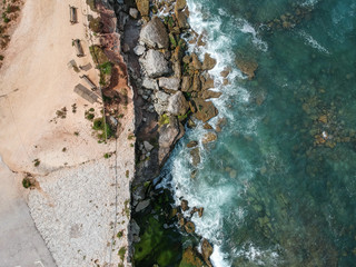 Aerial top view of sea waves hitting rocks on the beach with turquoise sea water. Amazing rock cliff seascape in the Portuguese coastline.