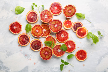 Sliced bloody oranges and mint leaves on a light gray surface.