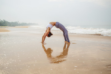 Caucasian woman practicing yoga at seashore of tropic ocean