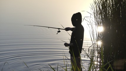 A man with a fishing rod on the shore of the lake is catching fish.
