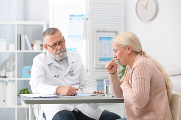 Coughing mature woman visiting doctor at clinic