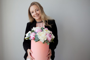Charming blonde woman with flowers in a hat box. Bouquet of peonies.
