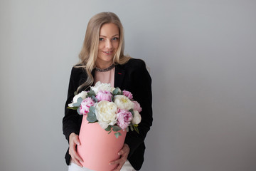 Charming blonde woman with flowers in a hat box. Bouquet of peonies.