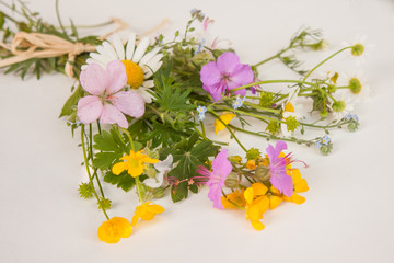 A colorful bouquet of freshly picked wild flowers from a natural meadow and garden tied with a natural decorative raffia string. Presented on a table outdoors on a white surface.