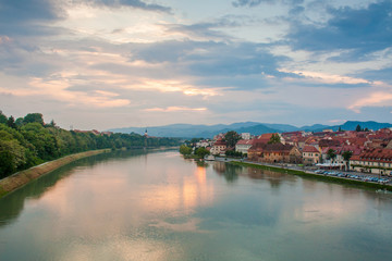 Fototapeta premium View of Maribor, Slovenia, Central Europe and the Lent area. Photo taken from Glavni most - bridge over the river Drava. Evening sky after sunset over colourful houses and a church in the distance.