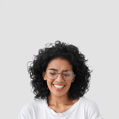 Vertical shot of overjoyed mixed race female laughs as watches comedy serial, has toothy smile,...