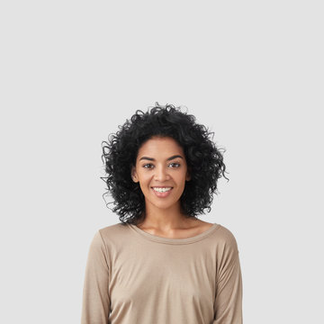 Smiling delighted young African American female has gentle smile, has white teeth, rejoices meeting with colleagues, dressed in casual clothes, isolated over white background with blank space