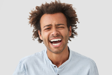 Optimistic glad African American male has broad smile, laughs at funny story, expresses positive...