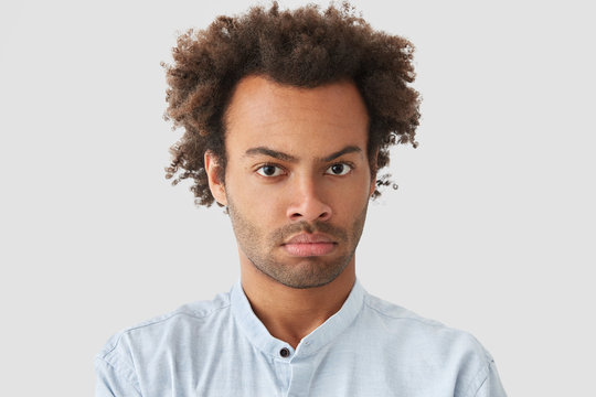 Headshot of attractive mixed race male boss, being discontent with startup project, looks seriously directly at camera, has Afro haircut, poses against white background. Facial expressions concept