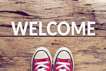 welcome sign text on wooden floor with red sneaker on it © asiandelight