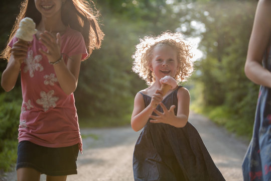 Little girl runinng with ice crem cone tryong to keep up with older girls