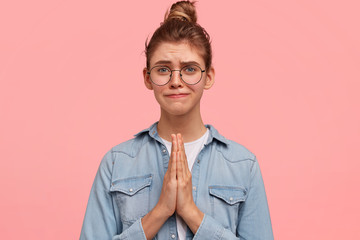 Photo of miserable pretty female makes praying gesture, keeps palms pressed together, has...