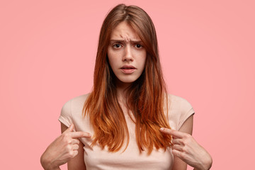 Candid shot of displeased Caucasian female frowns face, feels discontent after going shopping, bought t shirt of not good quality, indicates at blank space. People, clothing and emotions concept