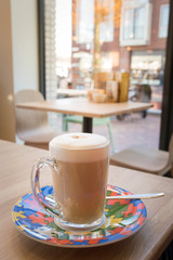 Cup of coffee on a wooden table in a drinking occasion with a modern design, the background look through a window just visible light of the morning sun.