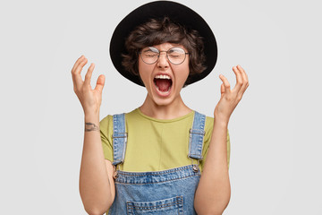 Furious angry young female feels hatred to someone, squalls and gestures in aggression while argues...