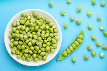 A white bowl filled with fresh peas, a number of scattered peas, photographed from above