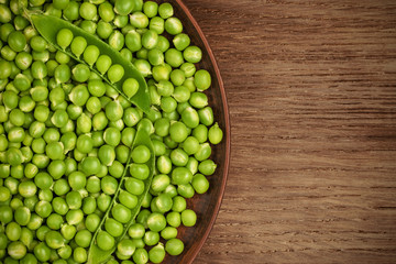 Two pods of green peas on a pile of peas in a plate. Place for text