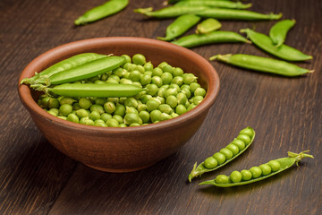 Harvest of freshly picked green peas in a bowl on a wooden rustic table