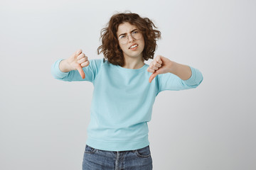 No, you have my rejection. Unsatisfied bothered girlfriend in stylish glasses and casual blue blouse, showing thumbs down, frowning, being displeased with idea, expressing dislike and negative answer