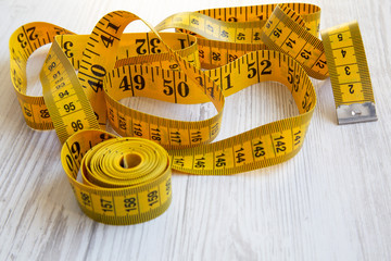 Yellow measuring tape on white wooden background, side view. Close-up.