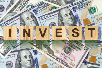Word, Invest composed of letters on wooden building blocks against the background of dollar bills. Concept business, finance.