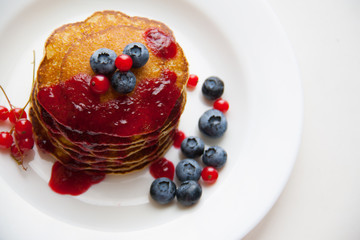 Homemade pancekes with fresh blueberries and red currants with cherry topping on white plate