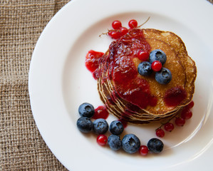 Homemade pancekes with fresh blueberries and red currants with cherry topping on white plate
