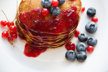 Homemade pancekes with fresh blueberries and red currants with cherry topping on white plate
