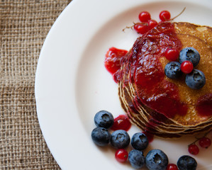 Homemade pancekes with fresh blueberries and red currants with cherry topping on white plate