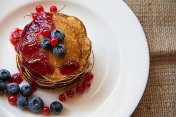 Homemade pancekes with fresh blueberries and red currants with cherry topping on white plate