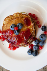 Homemade pancekes with fresh blueberries and red currants with cherry topping on white plate