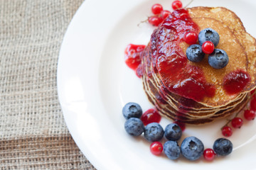 Homemade pancekes with fresh blueberries and red currants with cherry topping on white plate