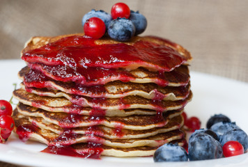 Homemade pancekes with fresh blueberries and red currants with cherry topping on white plate