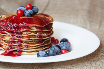 Homemade pancekes with fresh blueberries and red currants with cherry topping on white plate