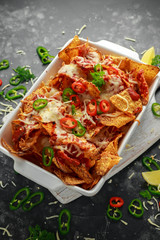 Maxican-style tortilla nachos chips topped with tomato salsa, sliced chilies and melted cheese served with lemon wedges and avocado yogurt dip