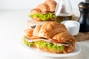 Fresh croissant or sandwich with salad, ham, jamon, prosciutto, salami, cheese, chicken, tomatoes on wooden background. Morning breakfast concept. Healthy and fast food.