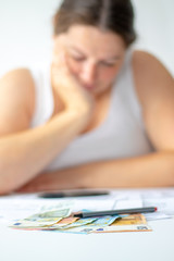 Obraz na płótnie Canvas Verzweifelte Frau hinter Ihrem Schreibtisch auf dem verschiedene Euro Geldscheine sowie ein Stift liegt