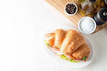 Fresh croissant or sandwich with salad, ham, jamon, prosciutto, salami, cheese, chicken, tomatoes on wooden background. Morning breakfast concept. Healthy and fast food.