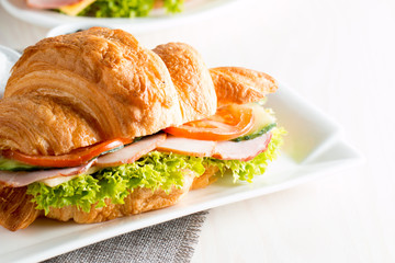 Fresh croissant or sandwich with salad, ham, jamon, prosciutto, salami, cheese, chicken, tomatoes on wooden background. Morning breakfast concept. Healthy and fast food.