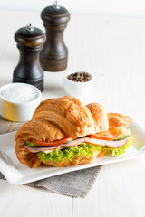 Fresh croissant or sandwich with salad, ham, jamon, prosciutto, salami, cheese, chicken, tomatoes on wooden background. Morning breakfast concept. Healthy and fast food.