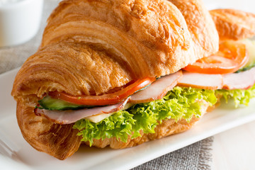 Fresh croissant or sandwich with salad, ham, jamon, prosciutto, salami, cheese, chicken, tomatoes on wooden background. Morning breakfast concept. Healthy and fast food.