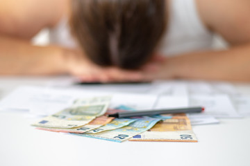 Verzweifelte Frau sitzt hinter ihrem Schreibtisch im B&uuml;ro auf dem verschiedene Euro Geldscheine liegen