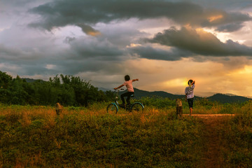 Two children playing paper airplane and ride bicycle on mountain at sunset