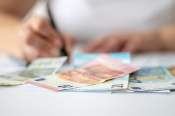 Euro Geldscheine auf einem Schreibtisch, hinter dem eine arbeitende Business-Frau sitzt