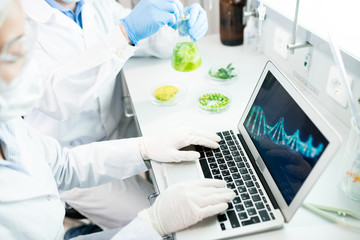 Crop view of microbiologists in laboratory clothes sitting at desk with samples of green vegetables...