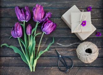Purple parrot tulips and craft gift box on rustic wooden background, Valentines Day or Mothers day background, top view. Gift box, ball of jute, flowers and retro scissors - set for gift wrapping.