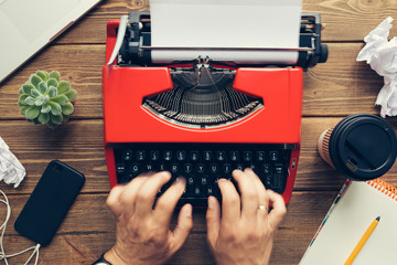 Top view close up of mans hands using vintage red typewriter placed on wooden desk