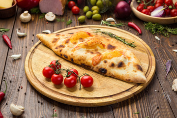 Traditional italian closed pizza Calzone with basil leaves on wooden background